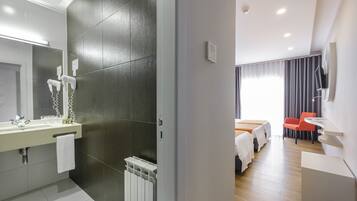 Una habitación de hotel moderna con un baño que cuenta con un espejo grande, un perchero para toallas y un secador de pelo. La habitación tiene una cama, un escritorio y una silla.