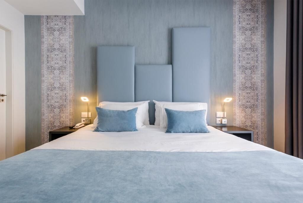 A hotel room with a large bed, two bedside tables with lamps, and a patterned wall.