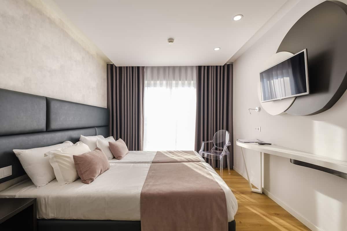 A modern hotel room with two beds, a TV, a desk, and a chair.