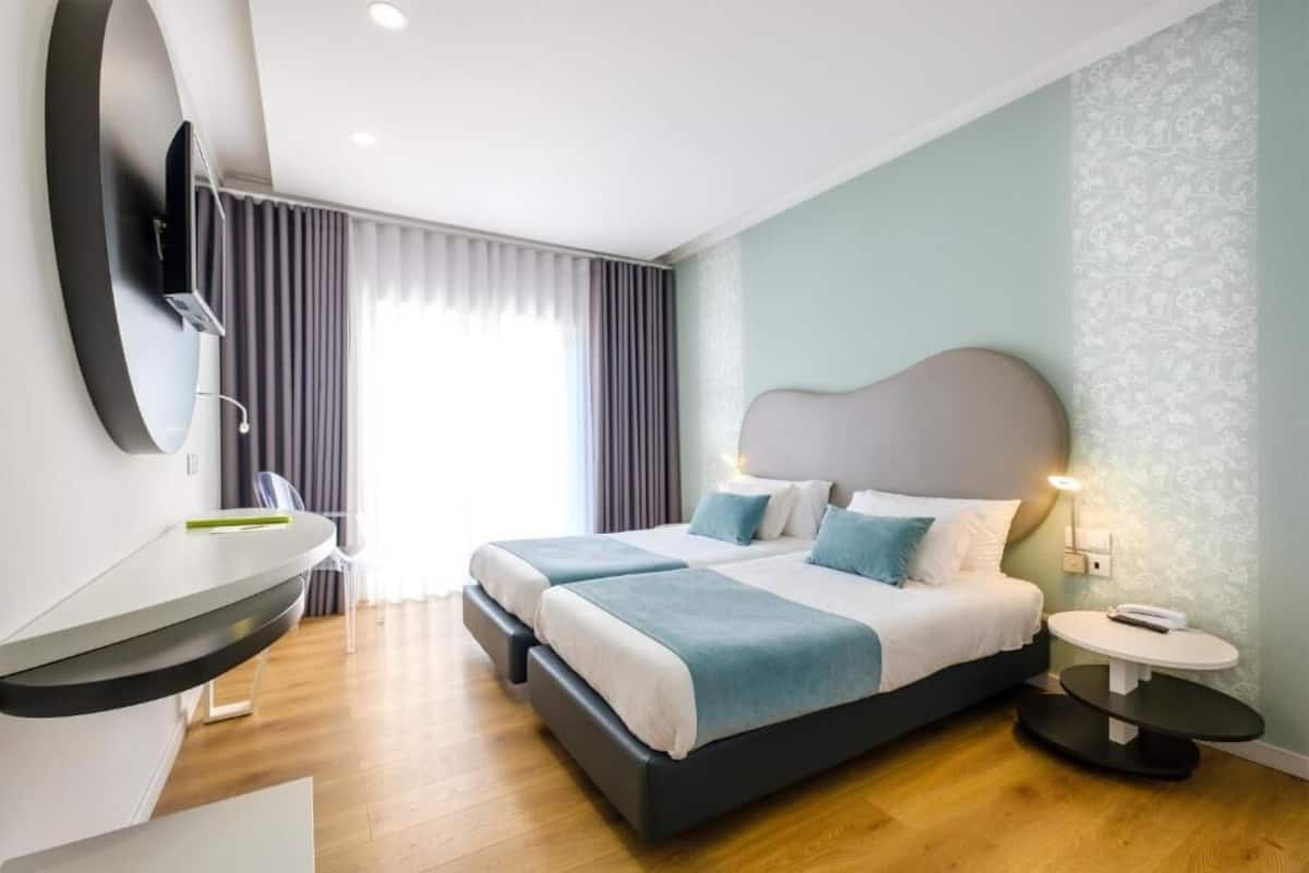 A modern hotel room with a large bed, bedside tables, a desk, and a TV mounted on the wall.