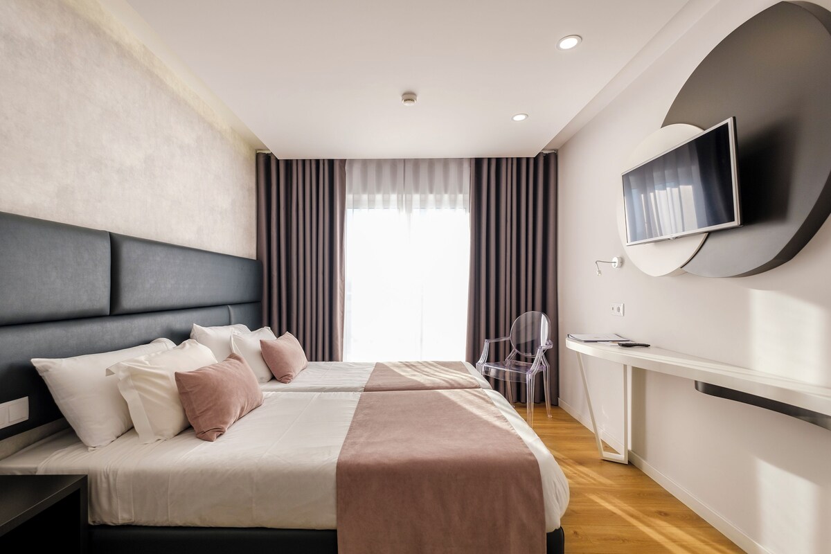 Una habitación de hotel moderna con una cama grande, un escritorio, una silla y un televisor montado en la pared.