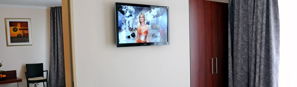 Una habitación con televisión de pantalla plana en la pared, una puerta de madera y una cortina estampada.
