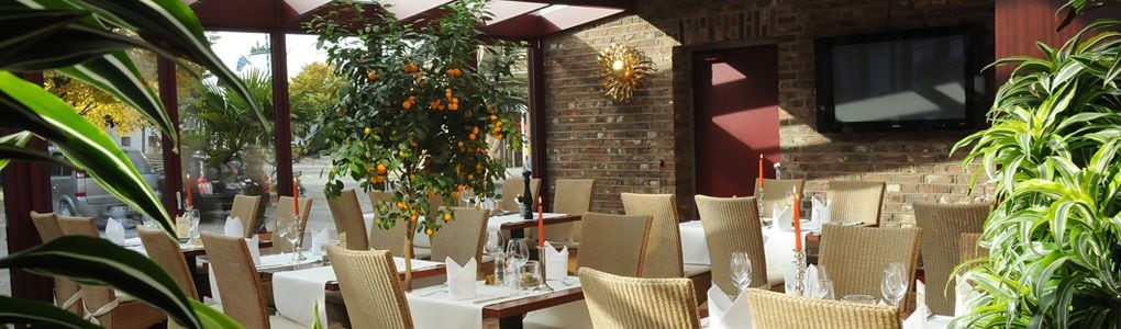 Un espace extérieur aménagé pour les repas, avec des chaises et des tables en osier, un mur en briques et un écran de télévision.