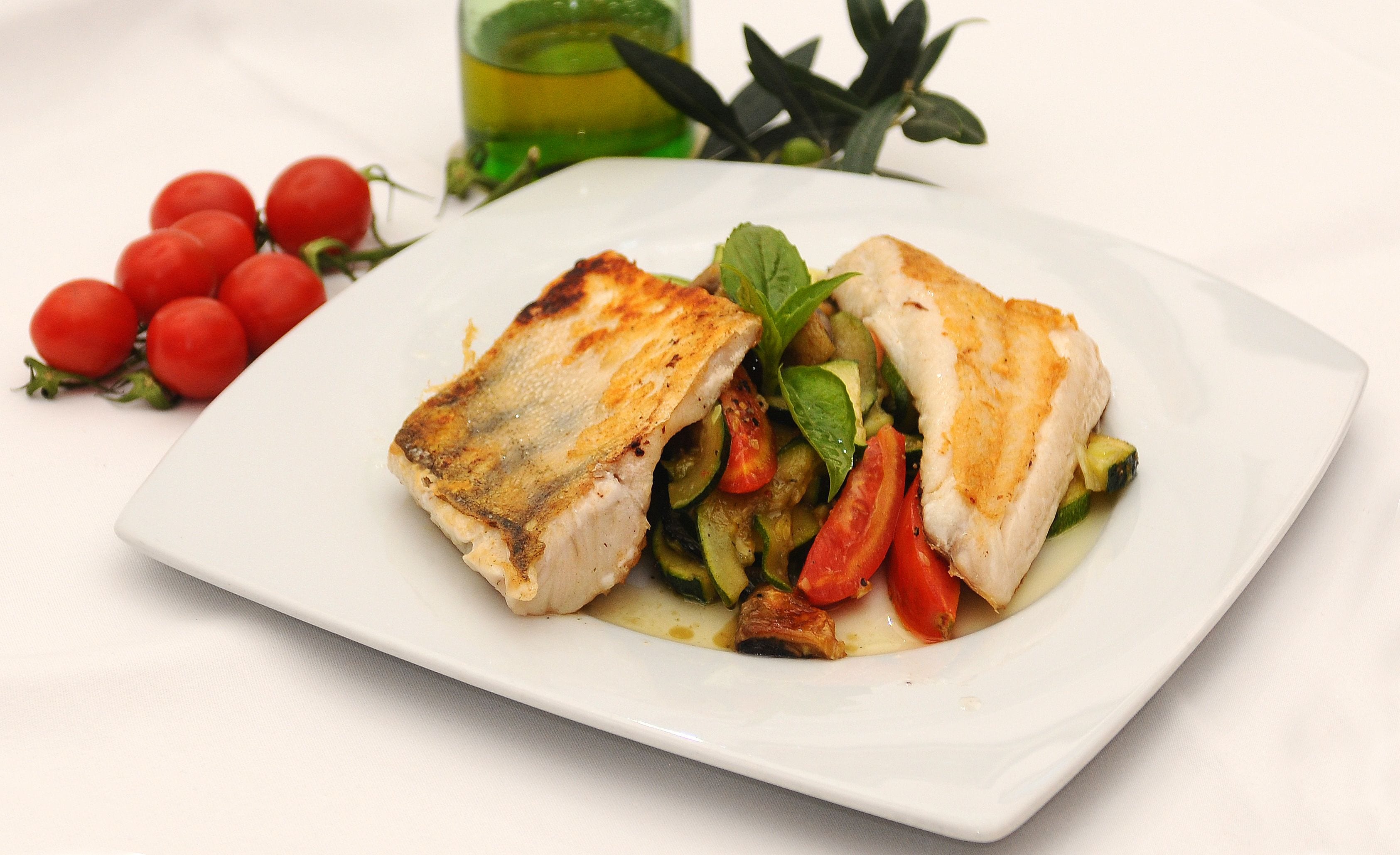 A white plate with a grilled fish fillet and vegetables.