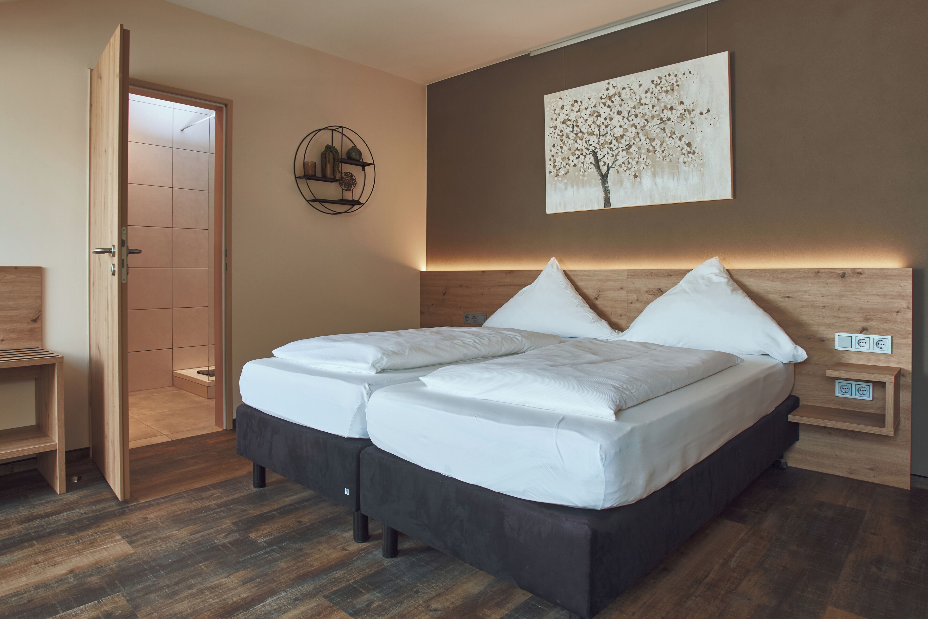 A modern bedroom with a large bed, a wooden headboard, a wall-mounted artwork, and a bedside table with a lamp.
