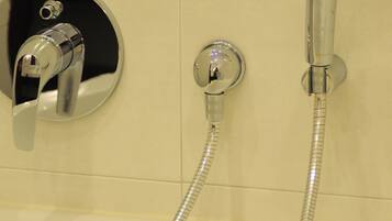 A bathroom with a bathtub, a handheld showerhead, and a wall-mounted faucet.