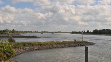 A river with boats, a rocky embankment, and a distant shoreline with trees.