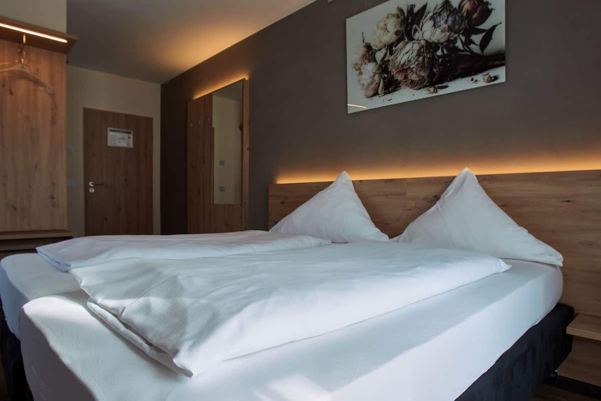 A neatly made bed with white linens, a wooden headboard, and a wall-mounted artwork.