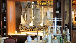 Een restaurantinterieur met een model schip, houten lambrisering en diverse flessen op planken.