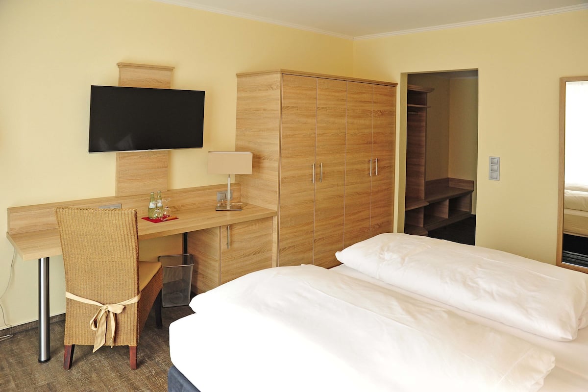 A hotel room with a bed, a desk with a chair, a TV, and a wardrobe.