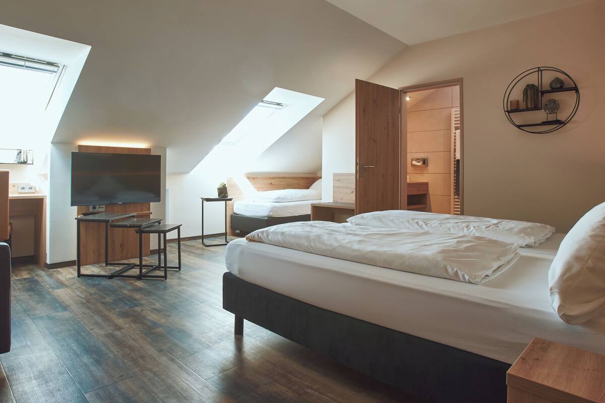 A modern bedroom with a large bed, a desk, and a skylight.