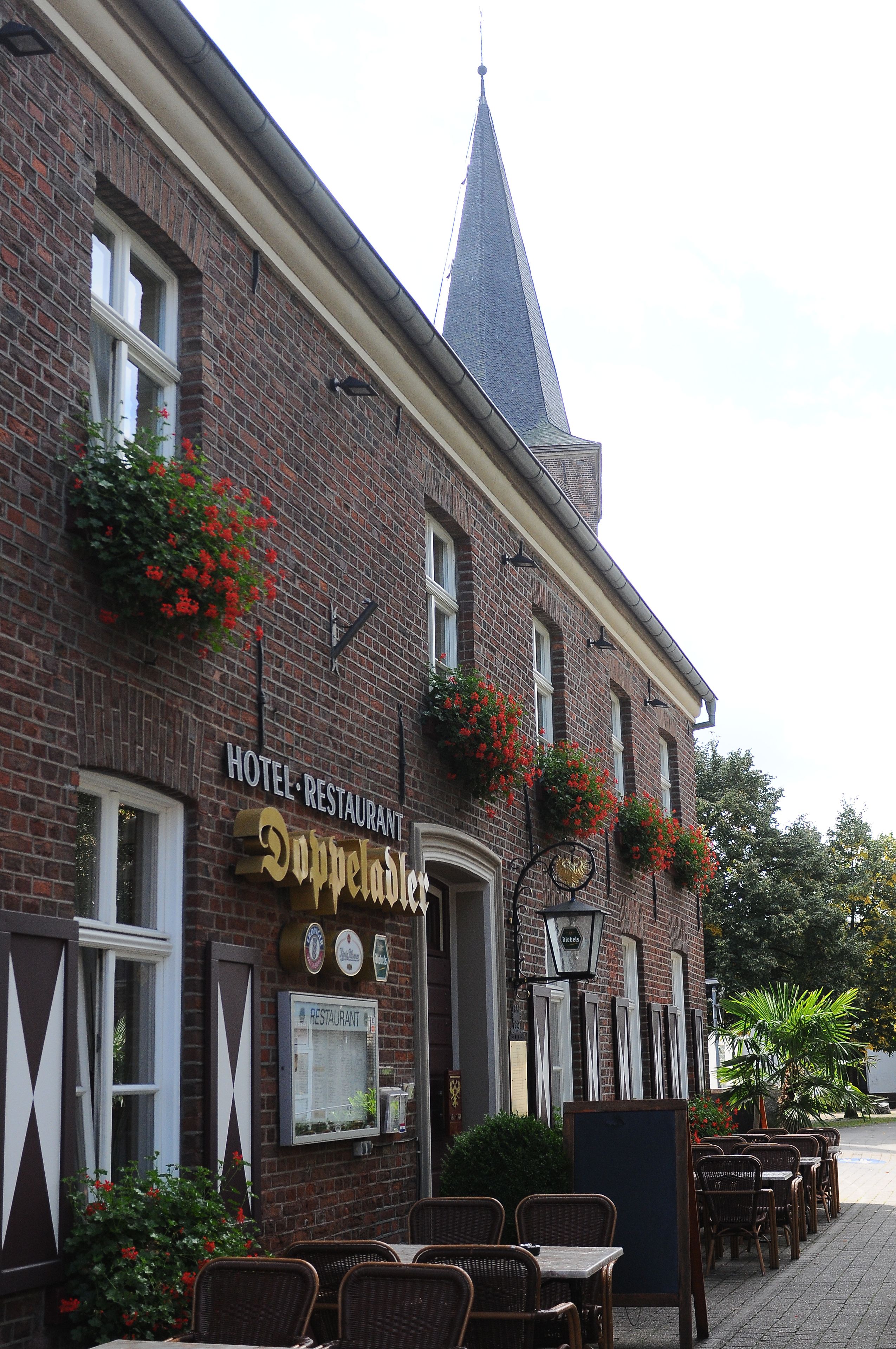 Un bâtiment en briques sur lequel on peut lire l’inscription « HÔTEL-RESTAURANT Dopperdaler ». Il y a des tables et des chaises à l’extérieur, ainsi que des jardinières sur les rebords des fenêtres.