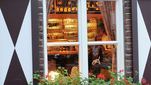 Een bakstenen gebouw met een etalage waar een bar en een persoon binnen zichtbaar zijn.