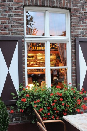 A brick building with a window displaying a bar and a person inside. - Hotel Restaurant Doppeladler (Rees)