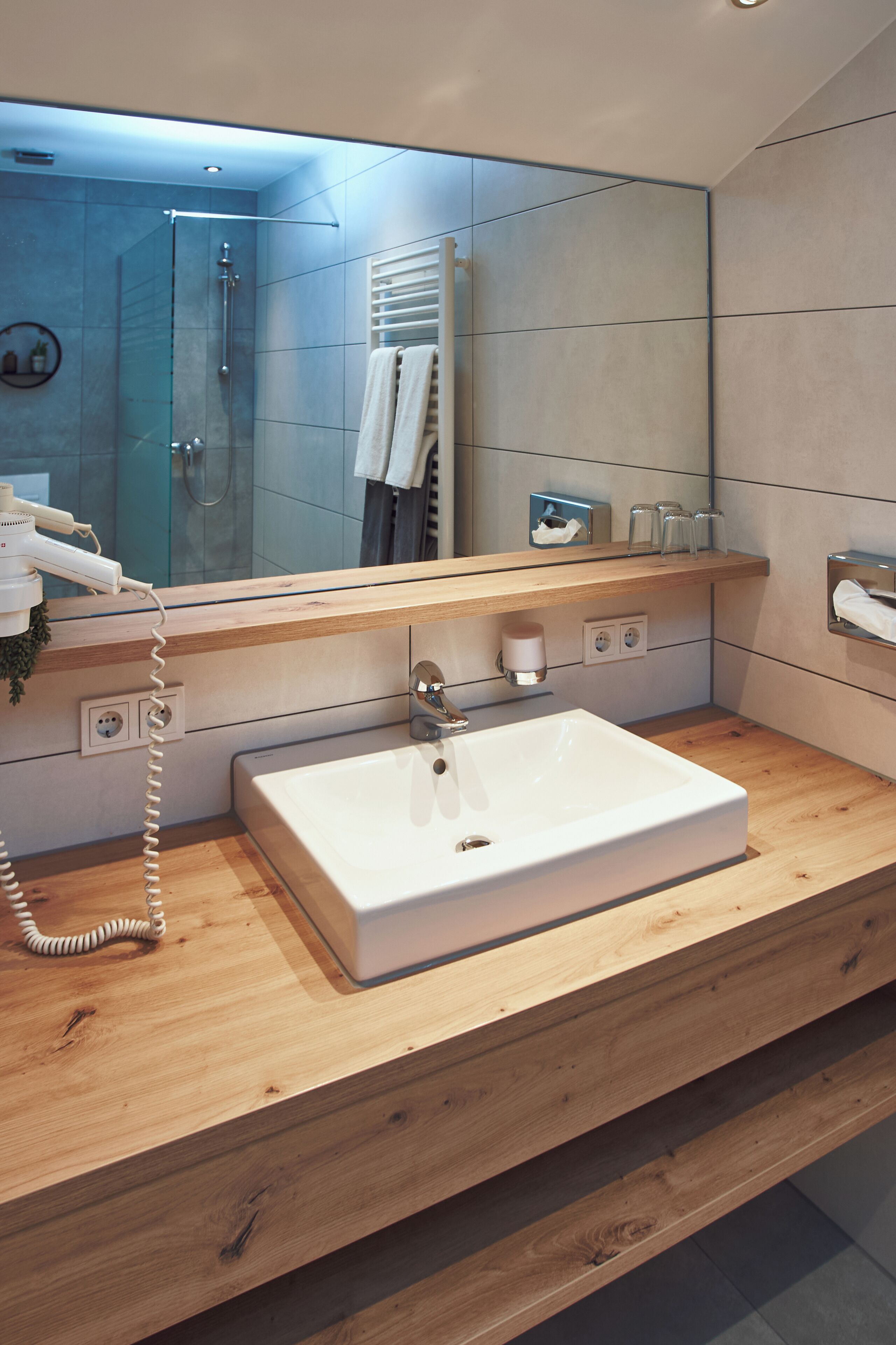 A modern bathroom with a large mirror, a white sink, and a hairdryer on the counter.