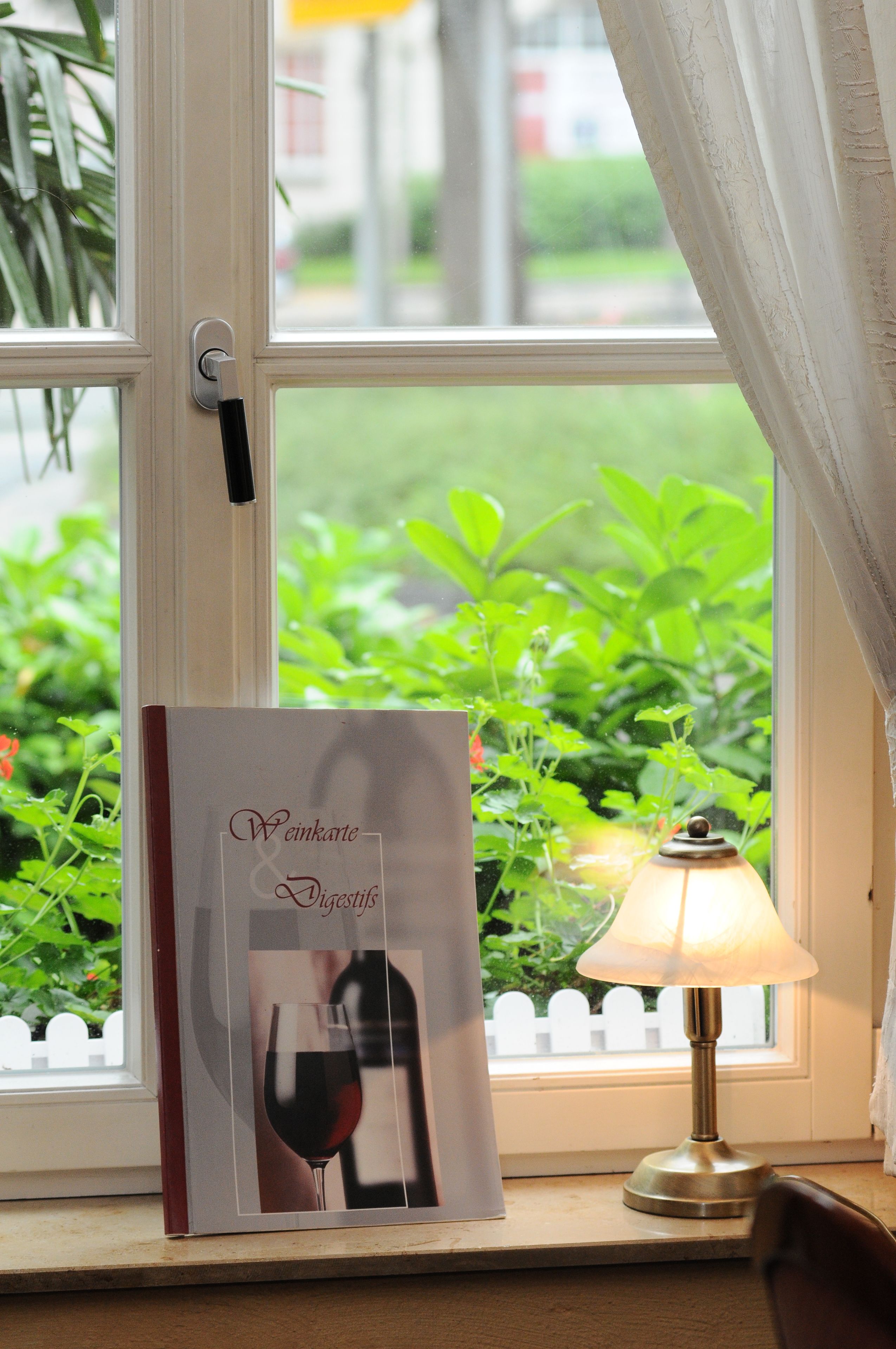 A window with a book titled "Weinkarte & Digestifs" and a table lamp on a windowsill.