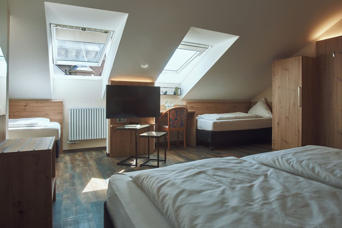 A modern, well-lit room with a sloped ceiling, skylights, a bed, a desk, and a chair.