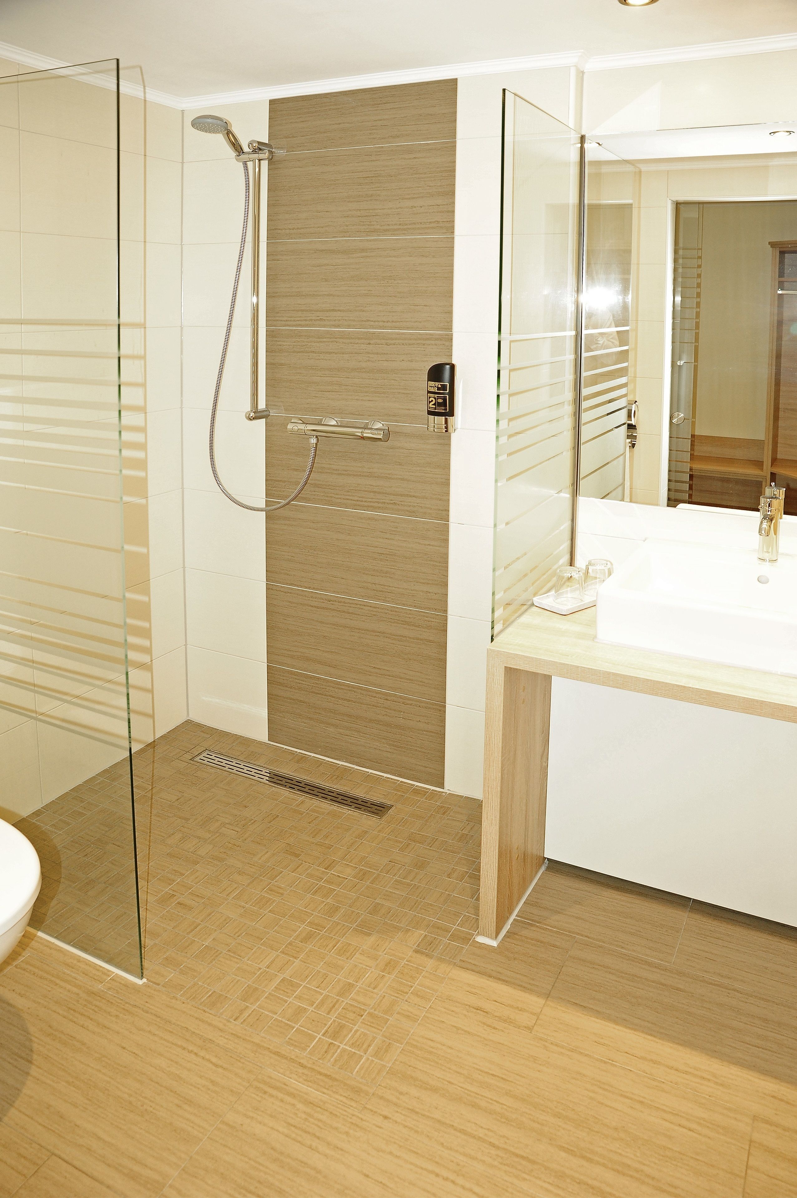 Une salle de bain moderne avec une douche à parois de verre, un meuble-lavabo en bois et un grand miroir.