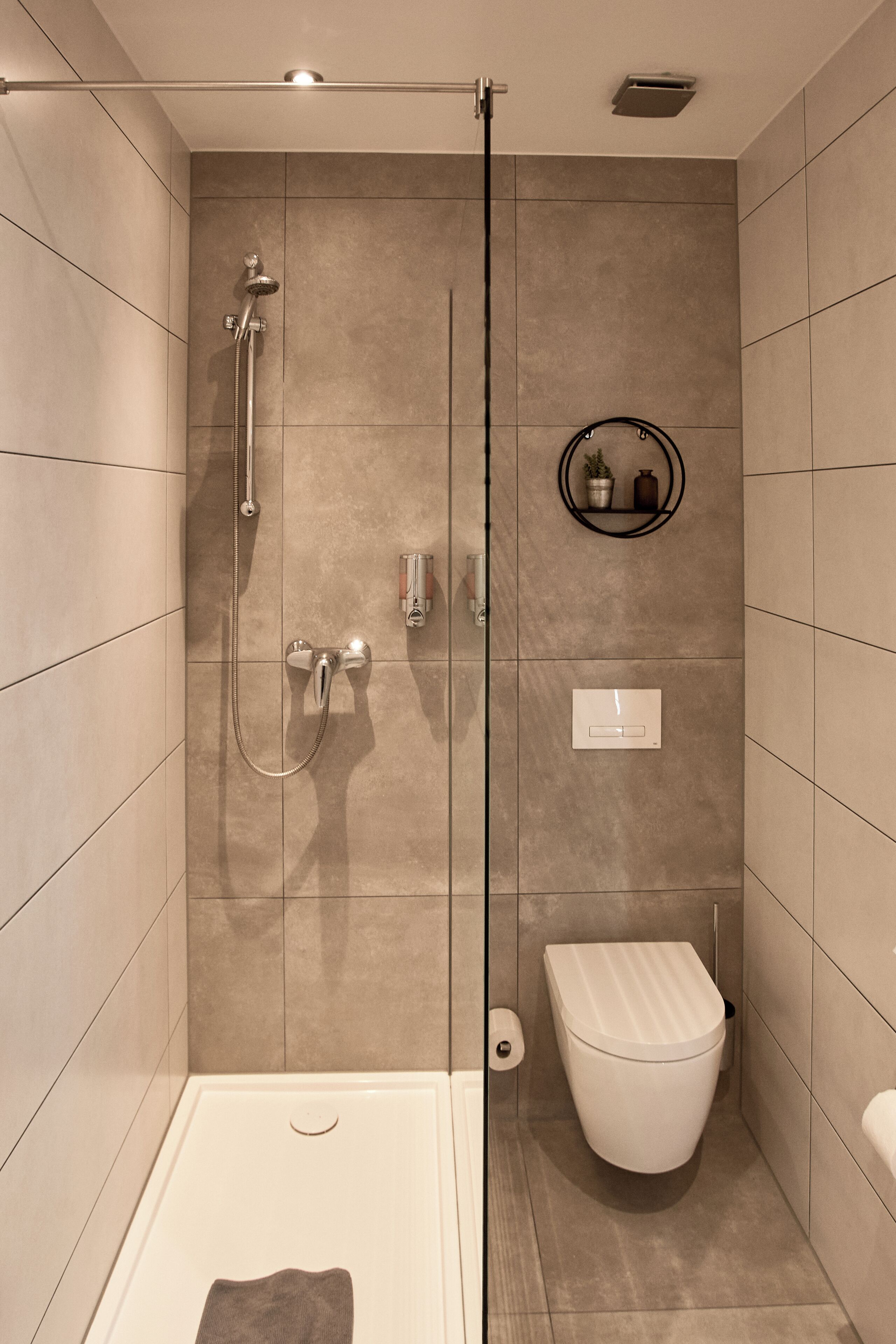 Une salle de bain moderne avec une douche à parois de verre, des toilettes et une petite étagère contenant des articles de toilette.