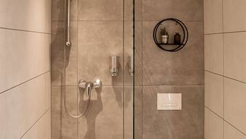 Une salle de bain moderne avec une douche à parois de verre, des toilettes et une petite étagère contenant des articles de toilette.