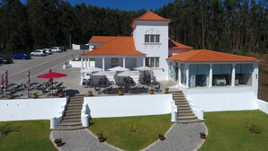 Um edifício branco com telhado de telhas vermelhas, mesas ao ar livre e área de estacionamento.