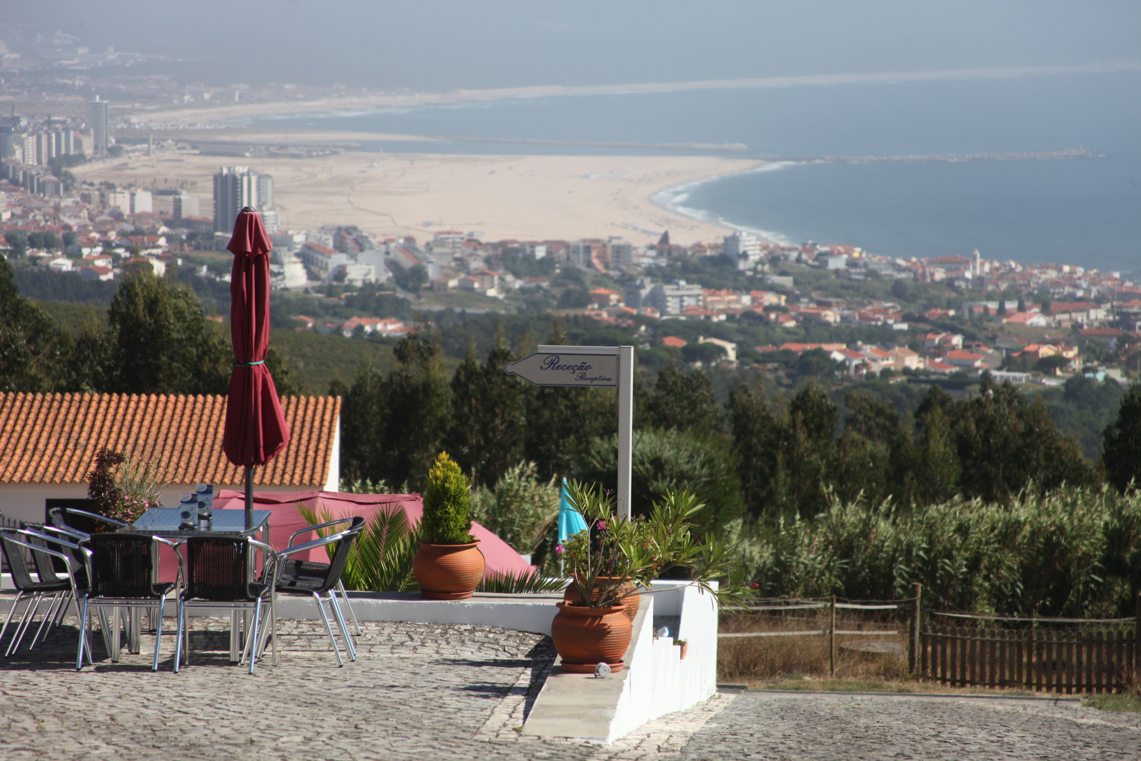 A patio area with outdoor seating, a view of a beach and cityscape, and a sign indicating a location.