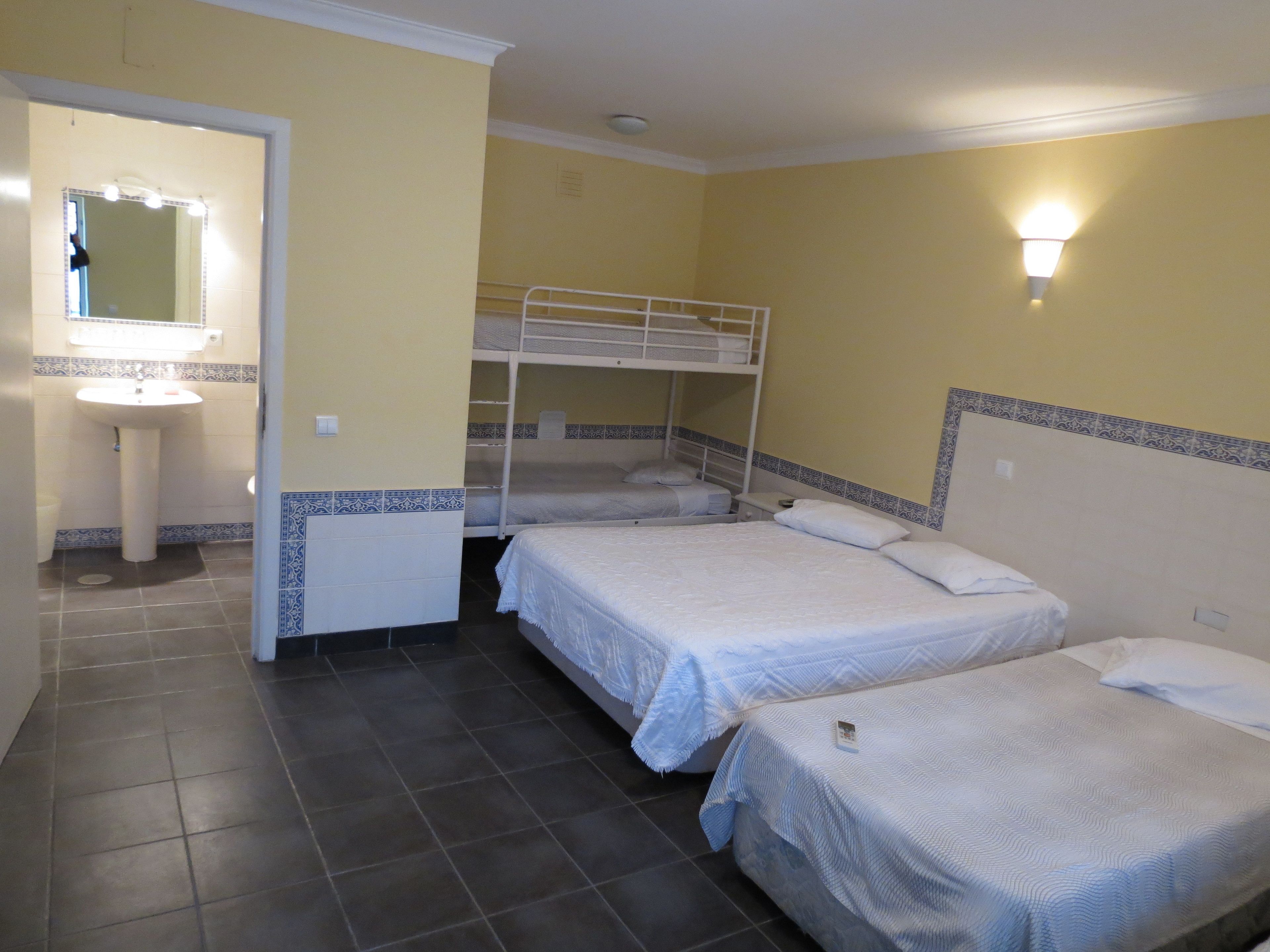 A room with two single beds, a bunk bed, a sink, and a mirror.