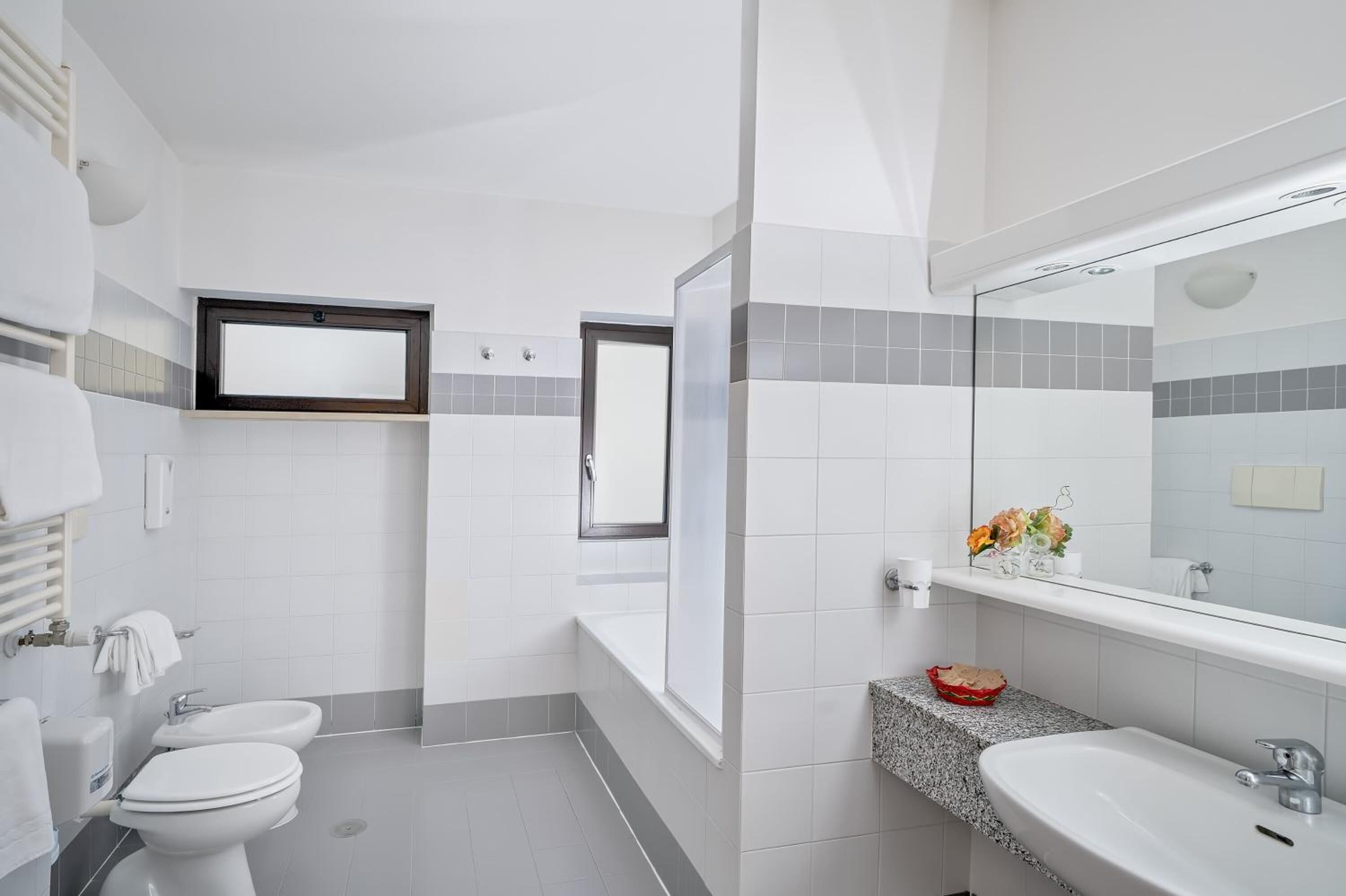A modern bathroom with white fixtures, a large mirror, and a granite countertop.