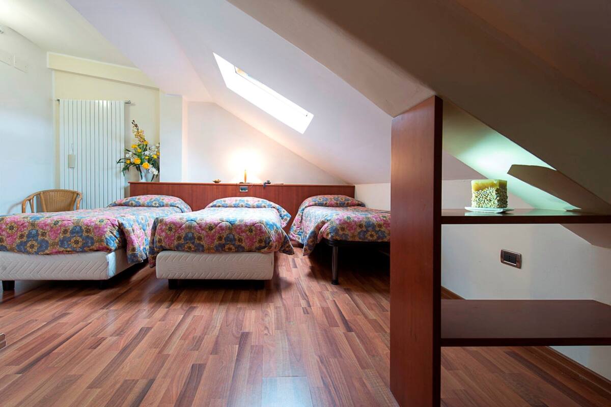 A bedroom with three beds, wooden flooring, a skylight, a radiator, and a small table with a plant.