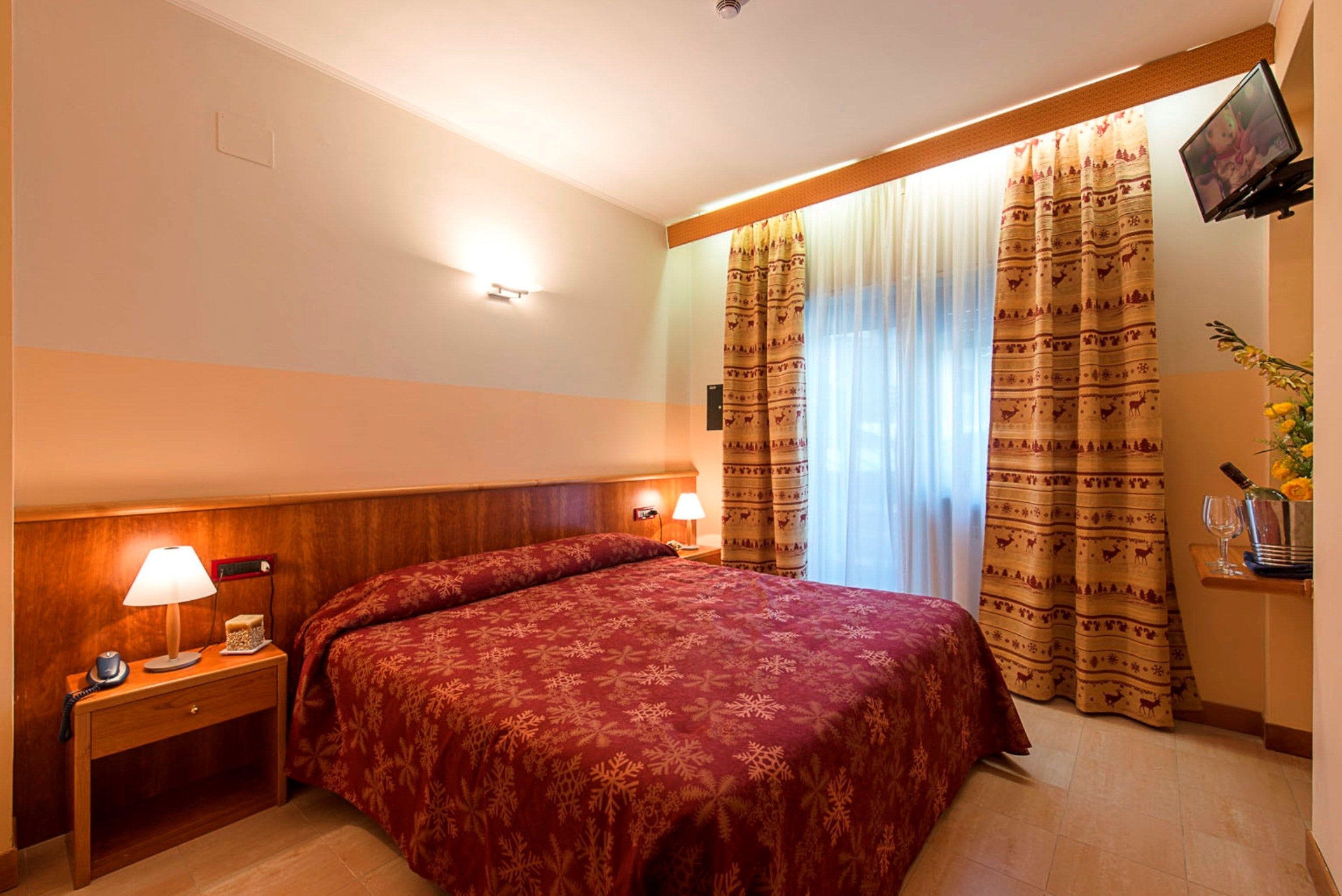 Une chambre d’hôtel avec un lit, des tables de chevet, des lampes, un téléviseur et des rideaux.