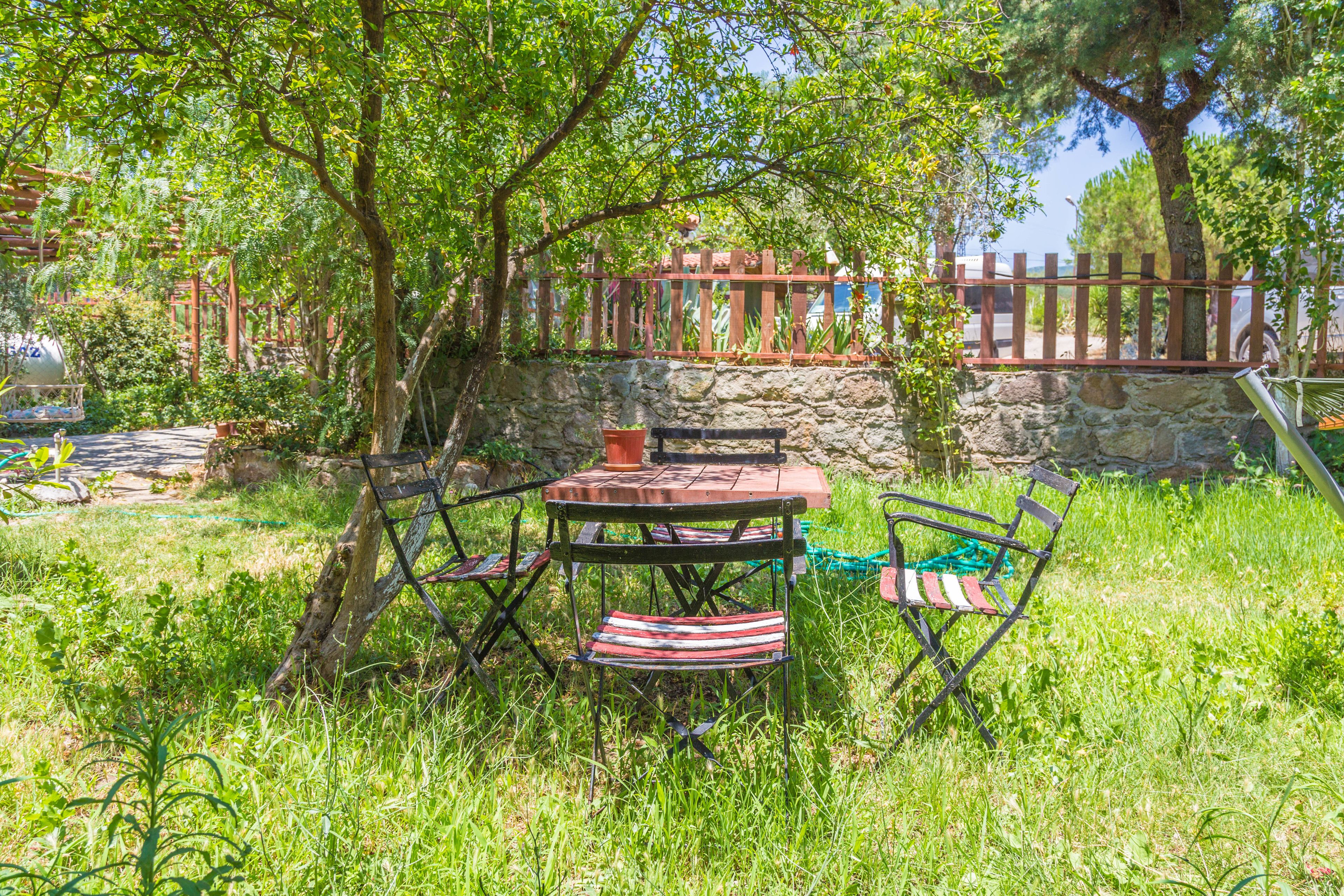 An outdoor seating area with a table and chairs, surrounded by greenery and a stone wall.