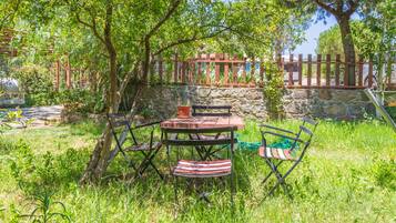 An outdoor seating area with a table and chairs, surrounded by greenery and a stone wall.