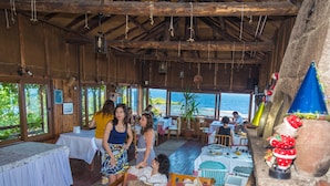 A rustic wooden interior with tables and chairs, large windows overlooking the sea, and a festive decoration. - Assos Terrace Hotel (Ayvacik)