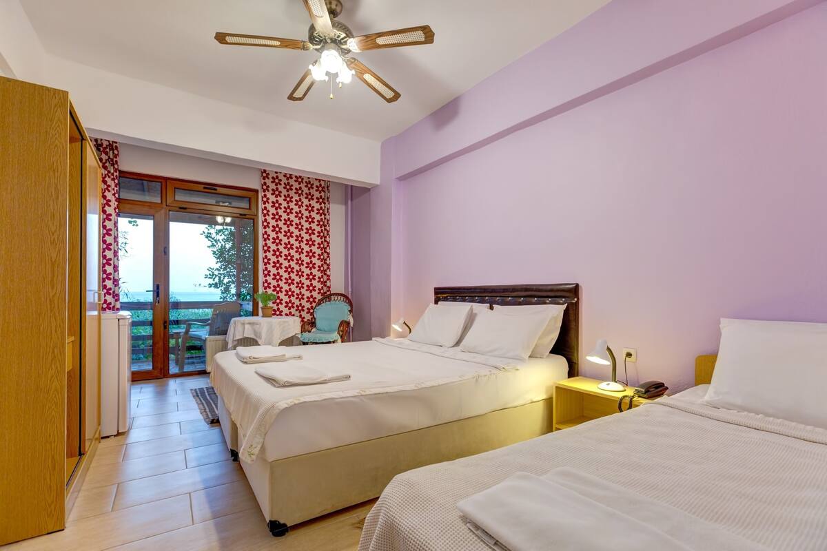Ein Schlafzimmer mit zwei Betten, einem Deckenventilator und Blick ins Freie.