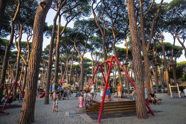 Un parque infantil con columpios y toboganes rodeado de árboles.
