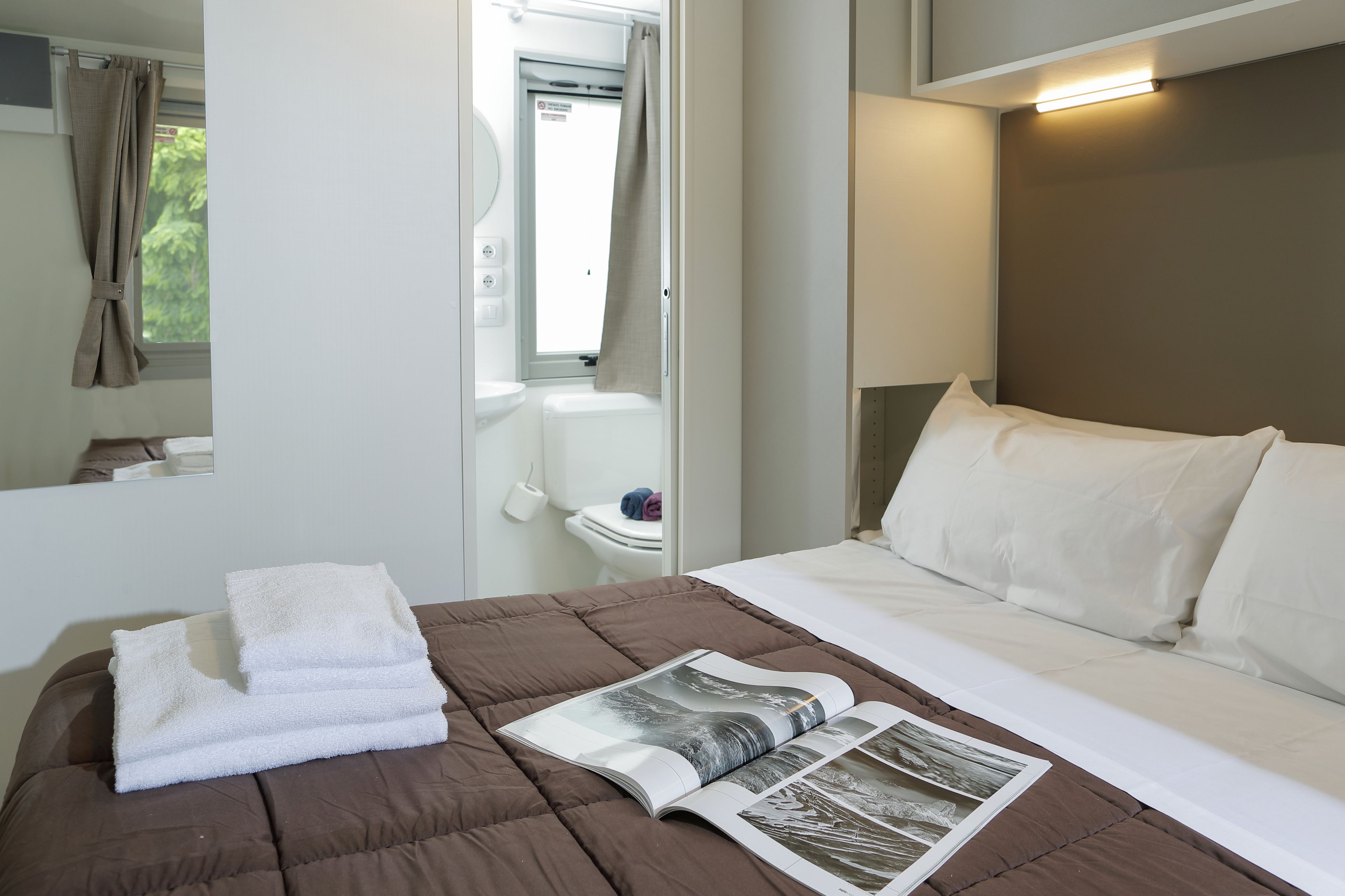 A neatly made bed with white linens, a brown bedspread, and a magazine on the bed.