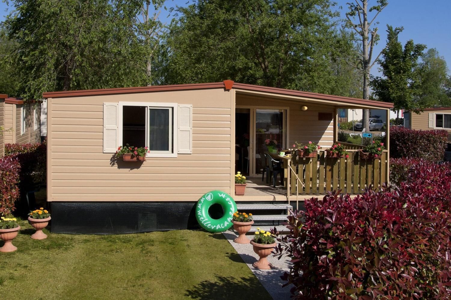 A mobile home with a front porch, a small deck, and a grassy yard.