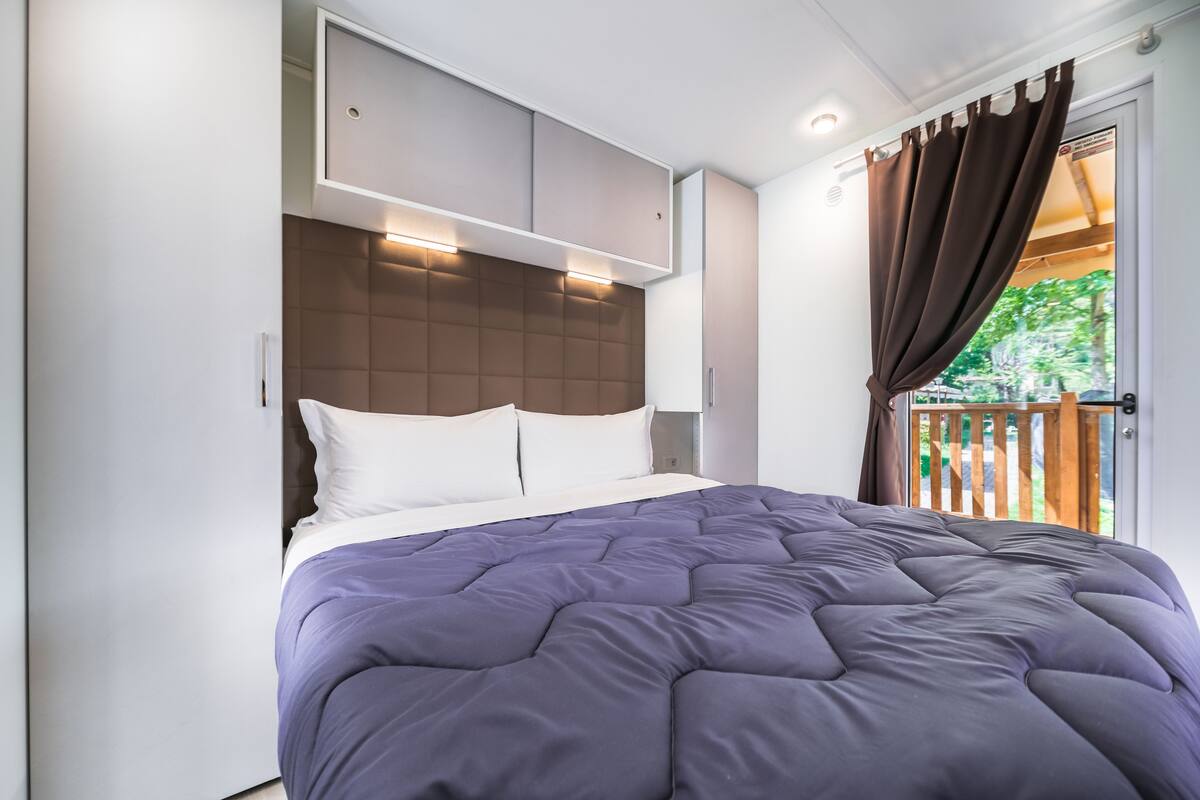 Un dormitorio con cama, cabecera y ventana con cortinas.