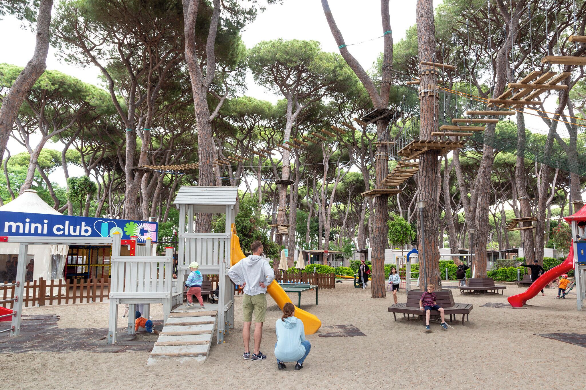 Un parque infantil con estructuras para escalar, bancos y una carpa que dice 'mini club'.