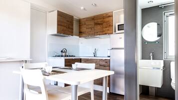 Eine moderne Küche mit weißen Schränken, einer Akzentwand aus Holz und einem Essbereich mit weißen Stühlen und einem Tisch.