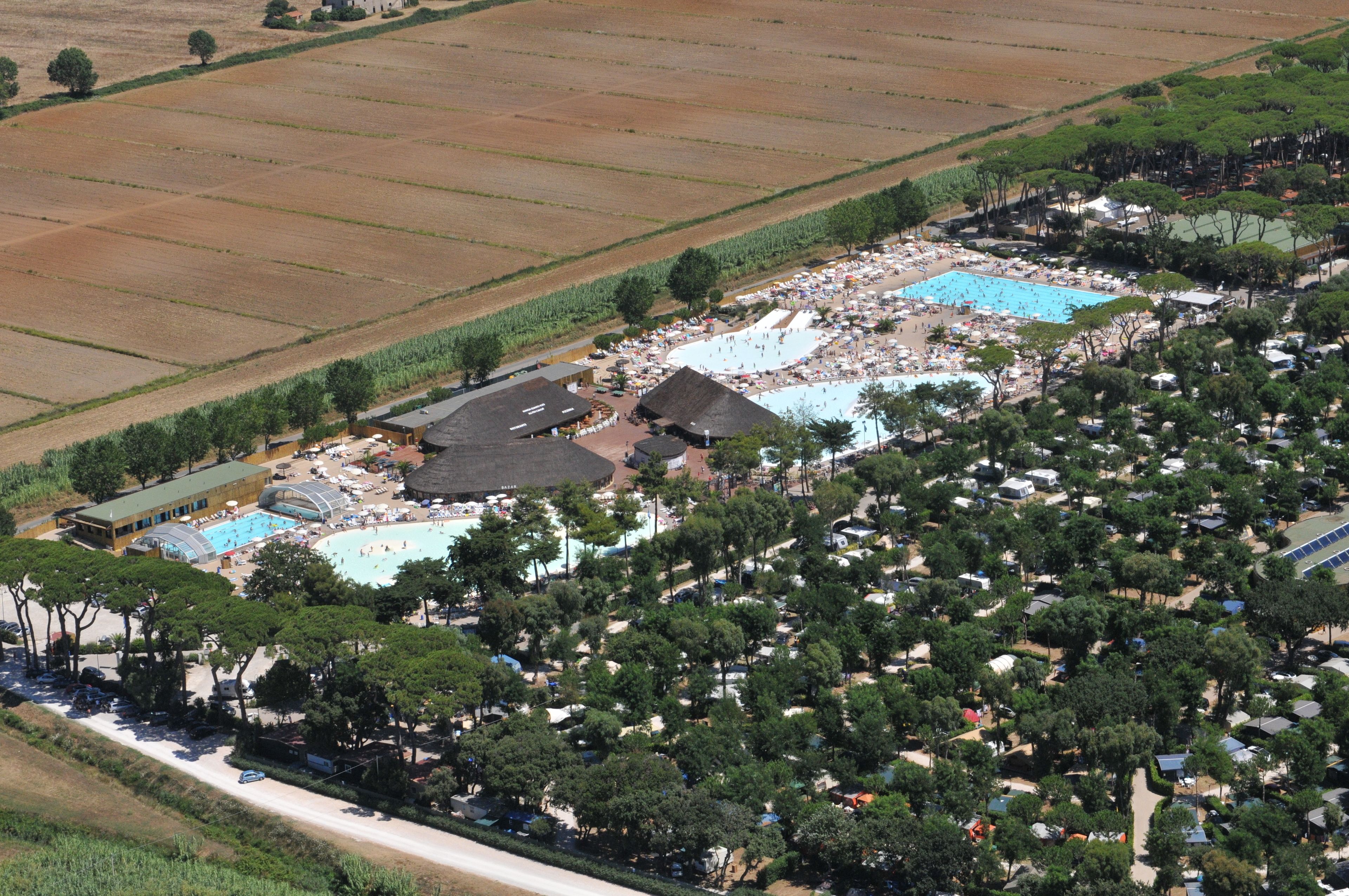 An aerial view of a resort with multiple swimming pools, beach areas, and dense tree coverage.
