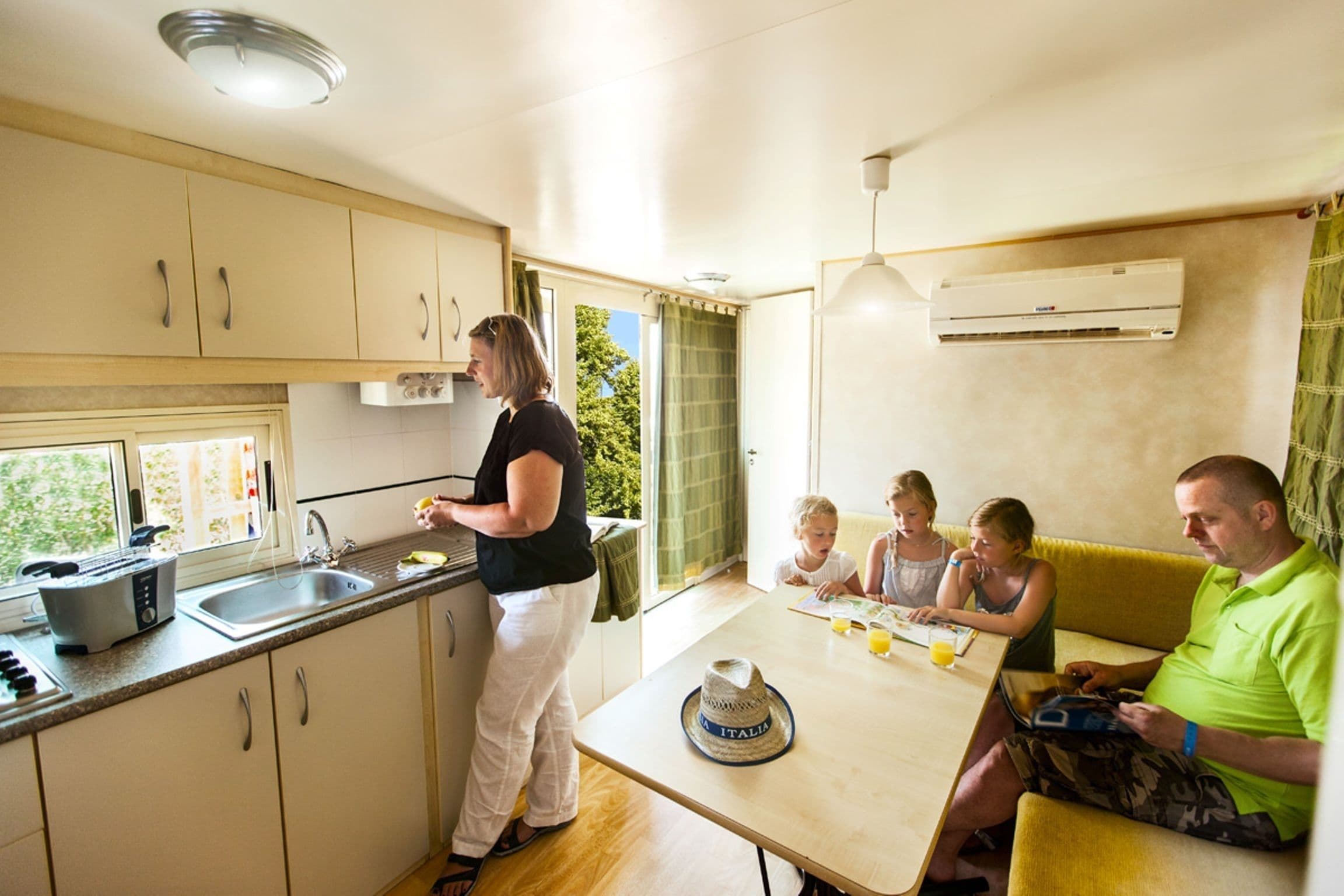 Una cocina con un lavamanos, una ventana y una mesa donde hay personas sentadas.
