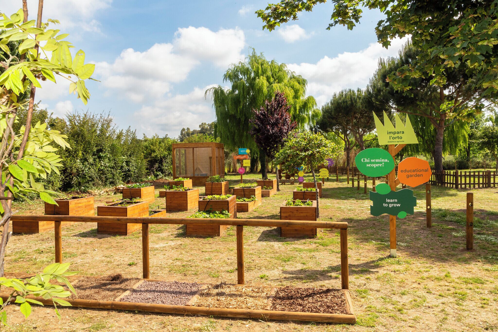 A garden with raised beds and a wooden structure, surrounded by trees and a clear sky.
