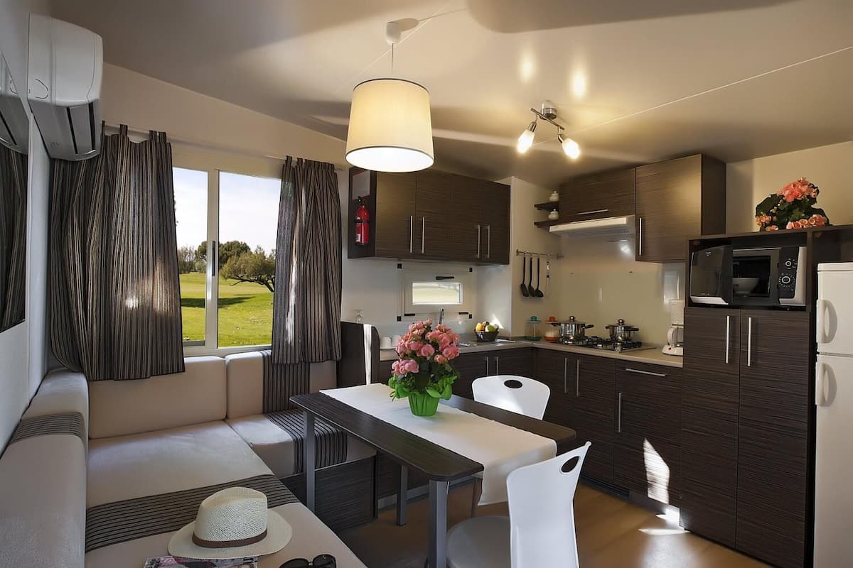 Una cocina moderna con armarios de madera oscura, un comedor con mesa y sillas, y vistas a un paisaje verde a través del ventanal.