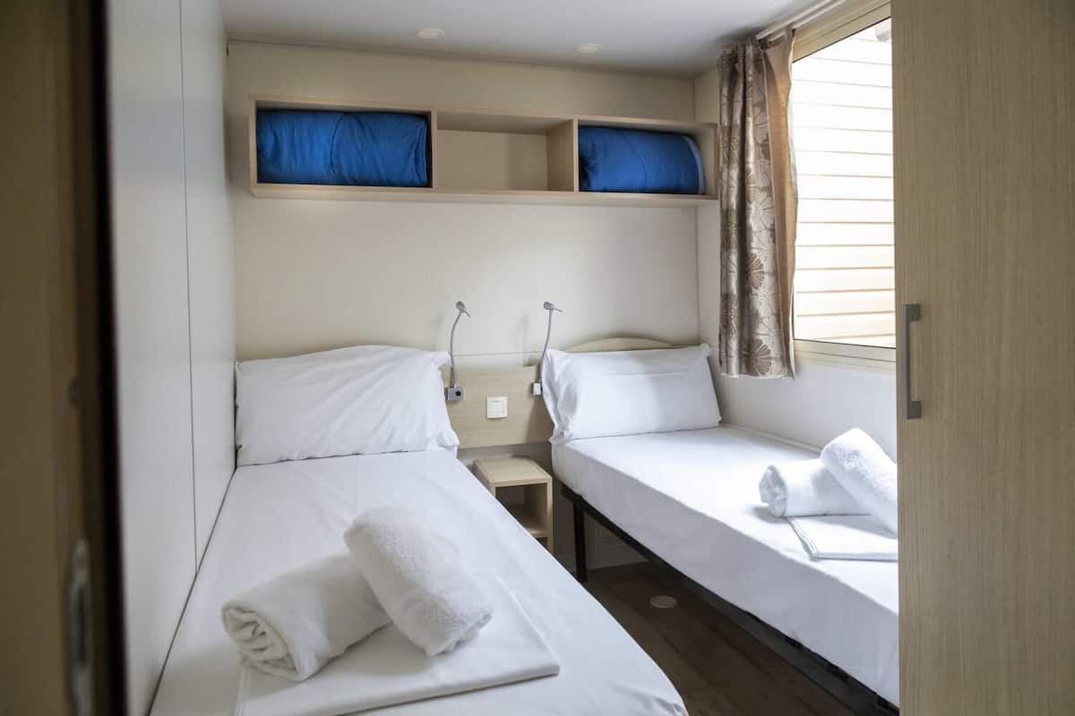 Una habitación de hotel pequeña con dos camas individuales, una mesita y una ventana con cortinas.