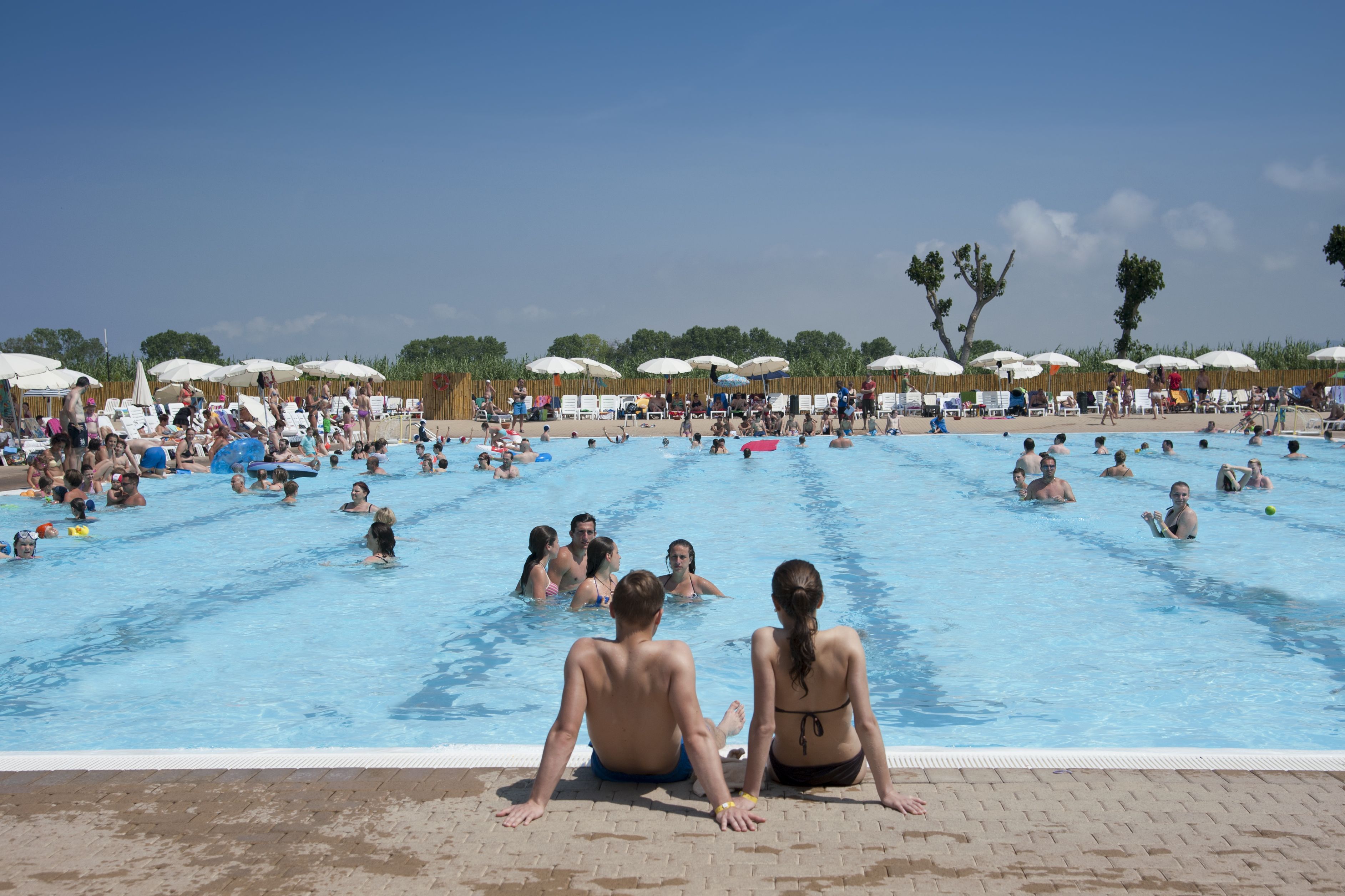 A large outdoor swimming pool with multiple lanes, surrounded by umbrellas and lounge chairs.