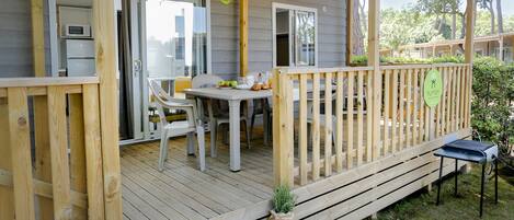 Une terrasse en bois avec une table et des chaises, un barbecue et un petit coin jardin.