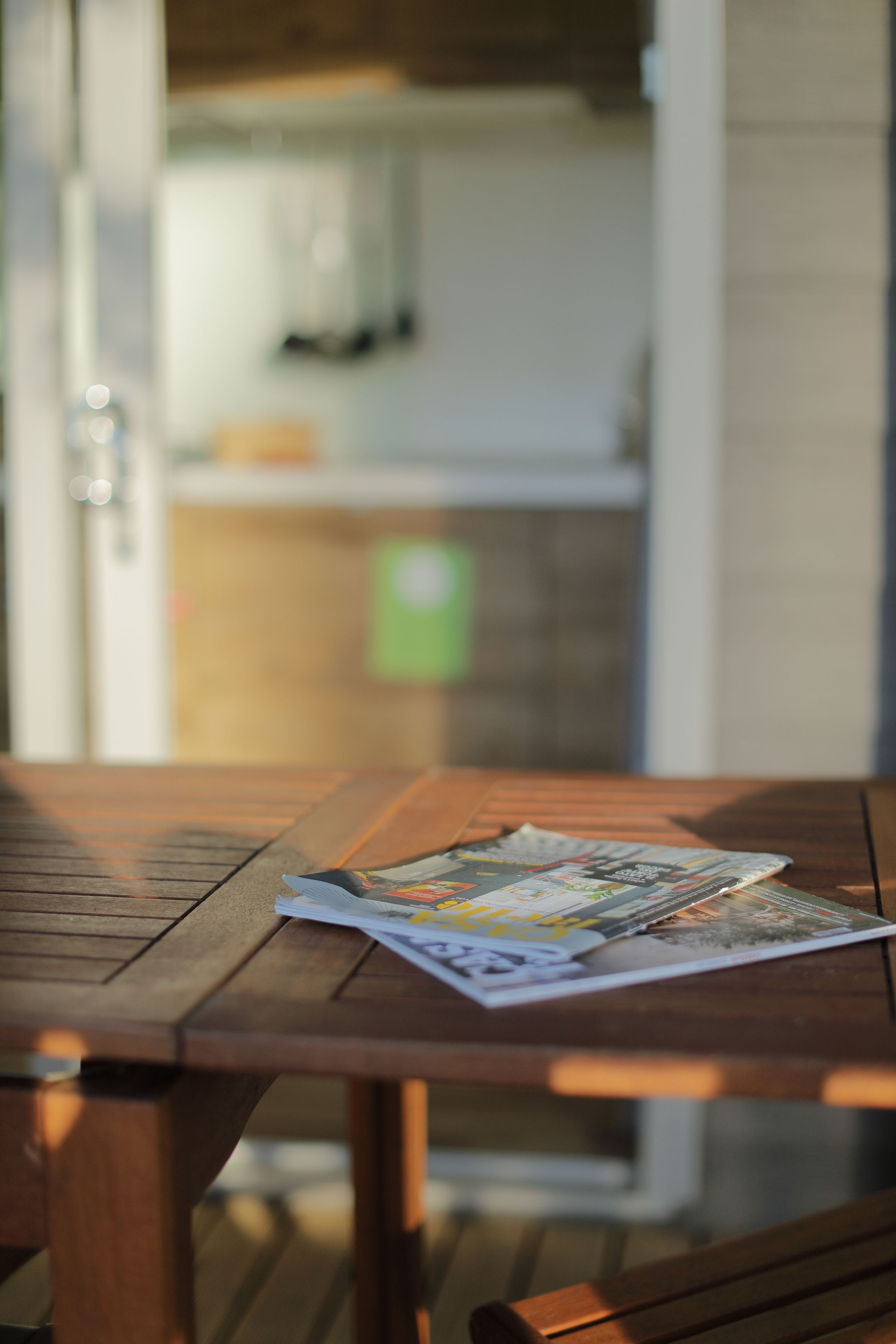 A wooden table with a magazine on it, in a room with a kitchen in the background.
