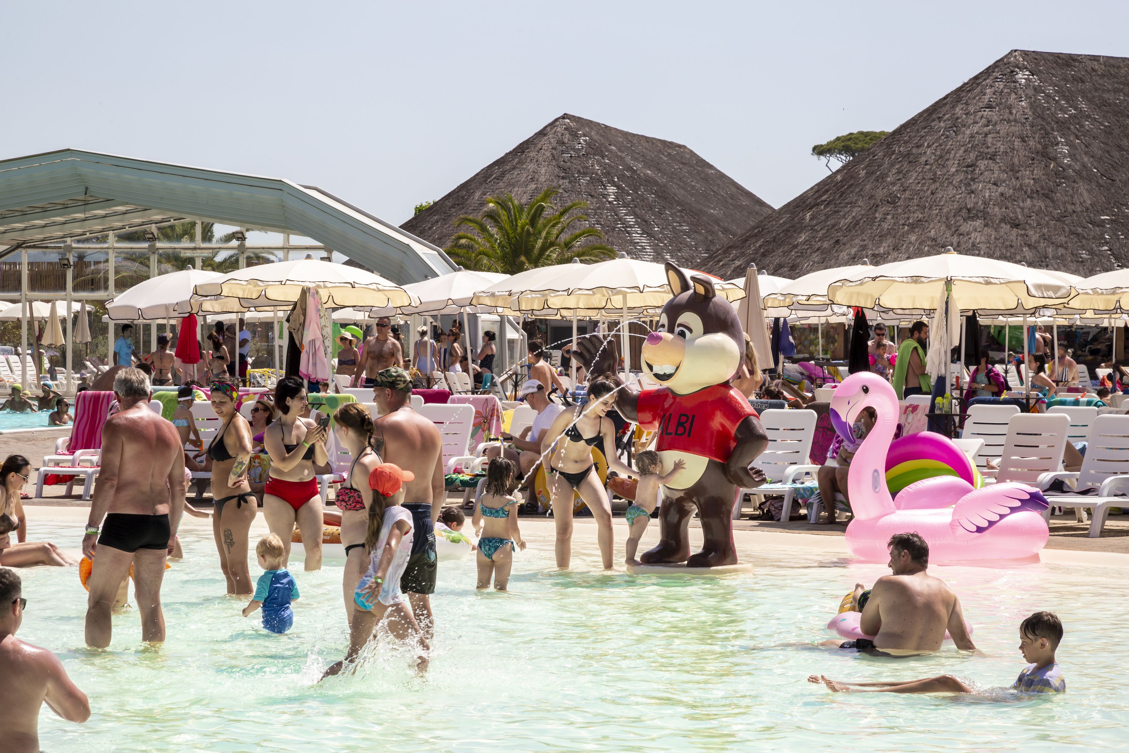Zona de piscina con gente, un personaje y juguetes inflables.