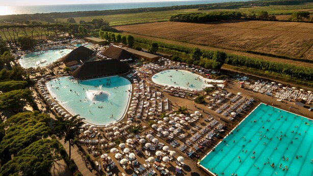 Ett flygbildsfoto av ett semesterområde med flera pooler, solstolar och parasoller.